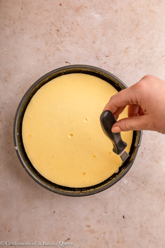 angled spatula loosening cheesecake from the springform pan on a light brown surface