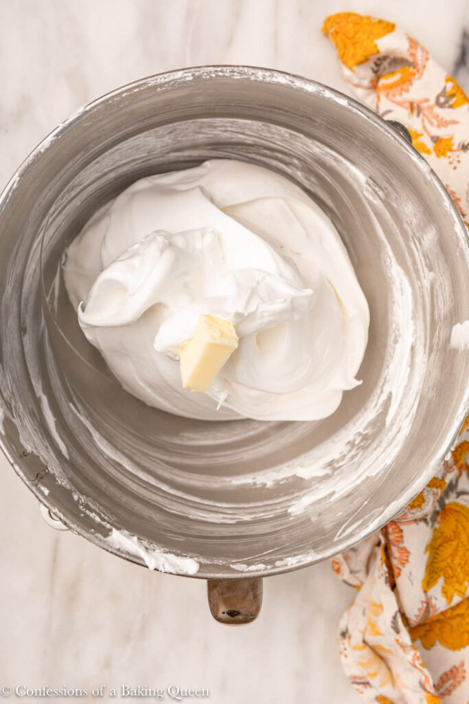 butter chunk added to meringue on a white marble surface with a floral linen