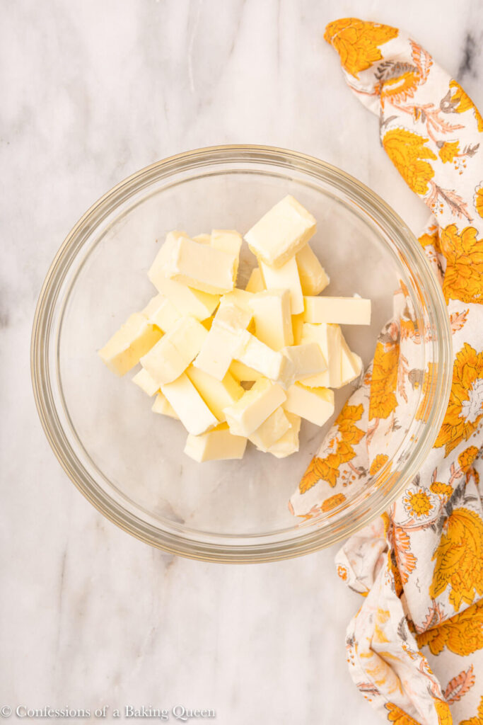 chunks of butter in an glass bowl on a white marble surface with a floral linen