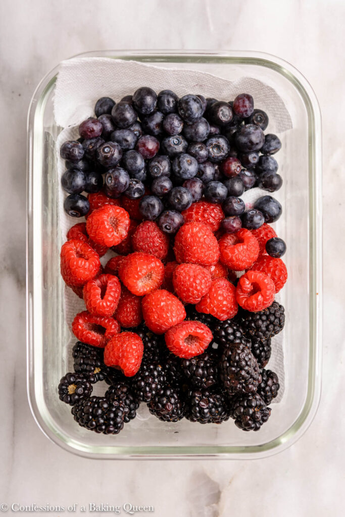 fresh berries washed and put in a paper towel lined glass container on a white marble surface