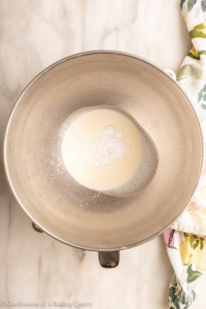 heavy whipping cream and confectioners sugar in a metal mixing bowl on a white marble surface with a floral linen