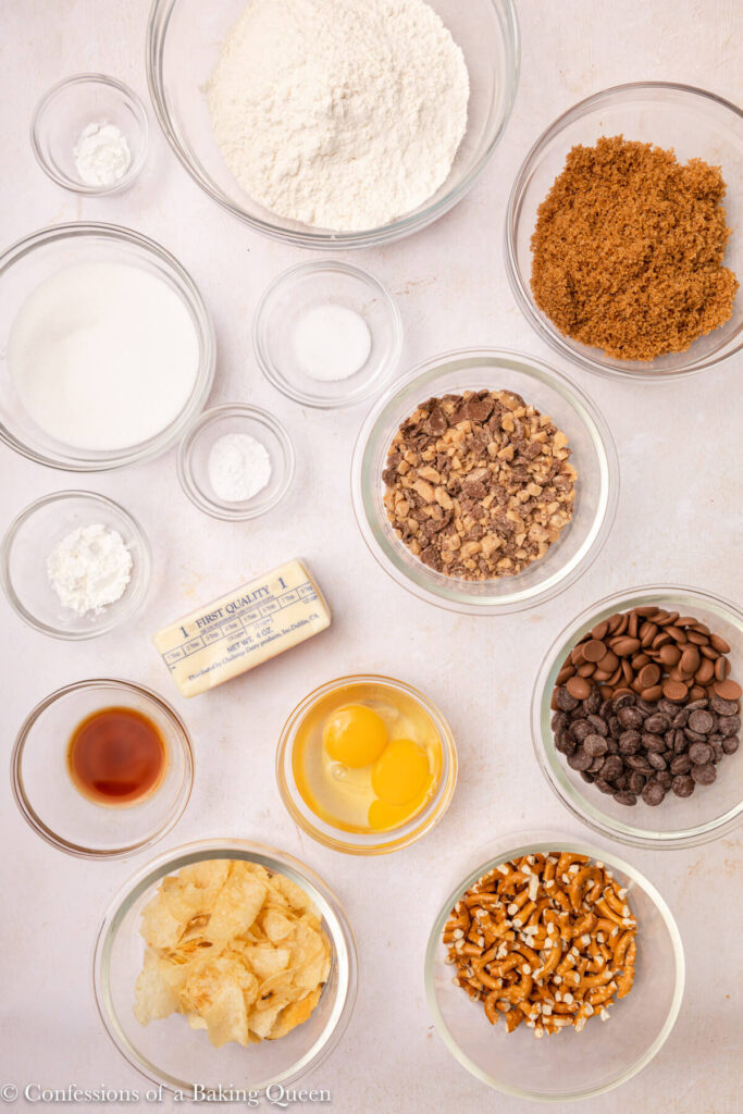 ingredients for kitchen sink cookies laid out in glass bowls on a light pink surface