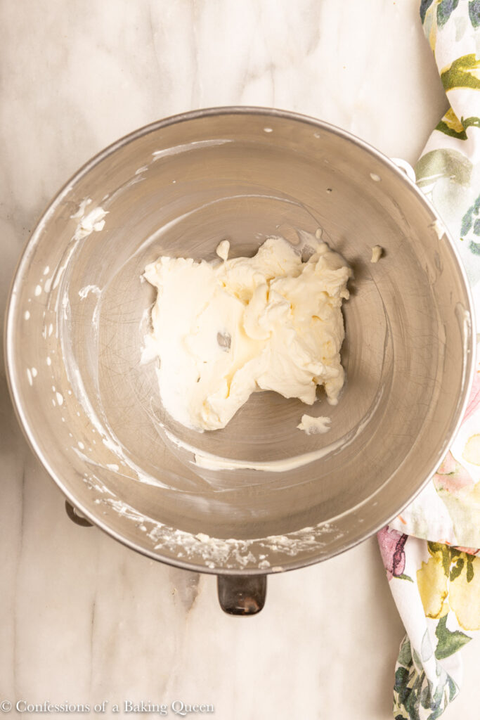 whipped cream in a large metal mixing bowl on a white marble surface with a floral linen