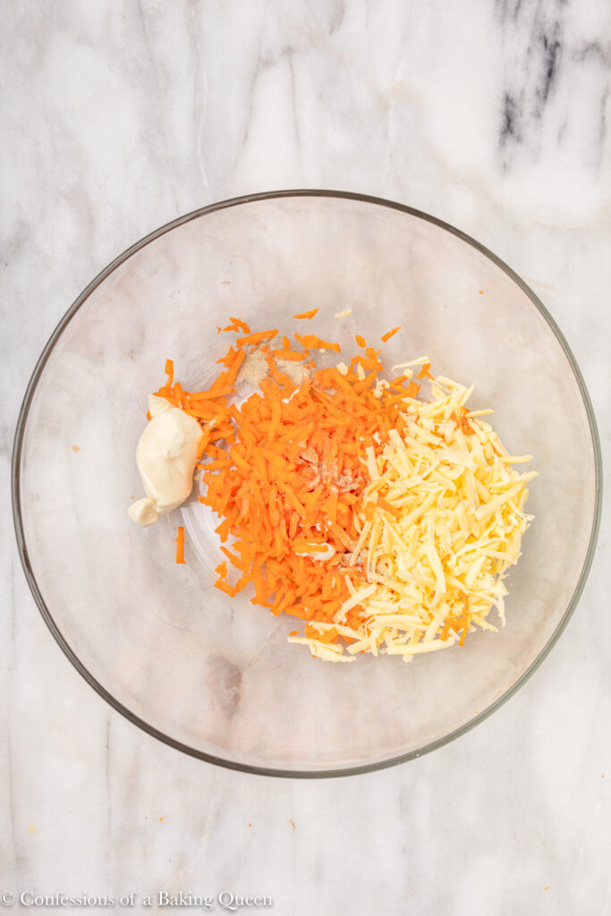 bowl of shredded carrots, grated cheddar cheese, mayonaise, and white pepper on a white marble surface