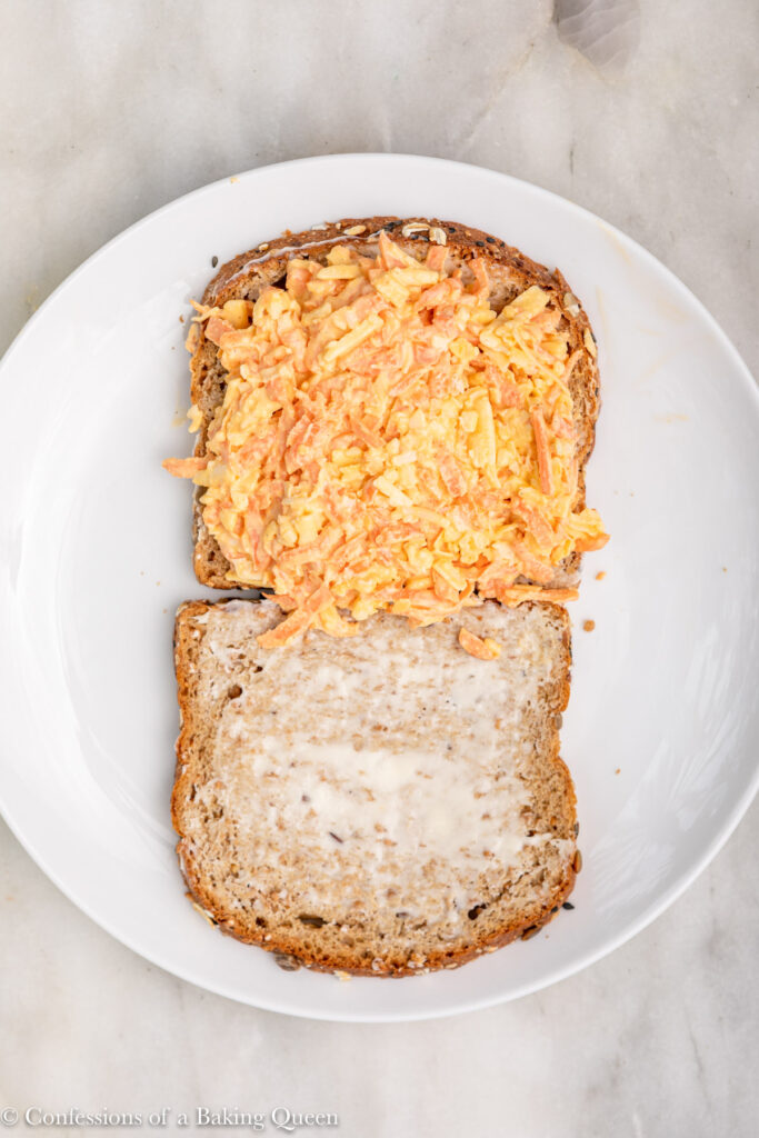 cheddar carrot sandwich filling added to a slice of buttered brown bread on a white plate on a white marble surface