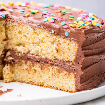 cut open yellow cake with chocolate frosting on a white plate on a white marble surface
