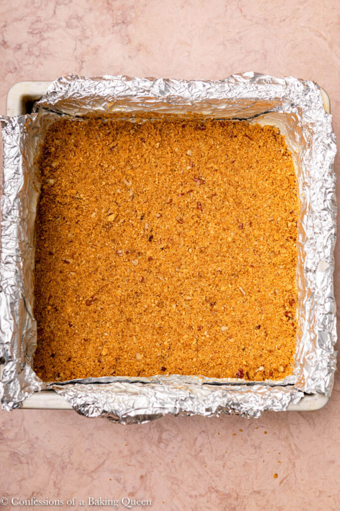 pecan graham cracker crust pressed into a square pan on a light brown surface