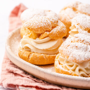 cream puffs dusted with confectioners sugar served on a light pink plate on a white surface