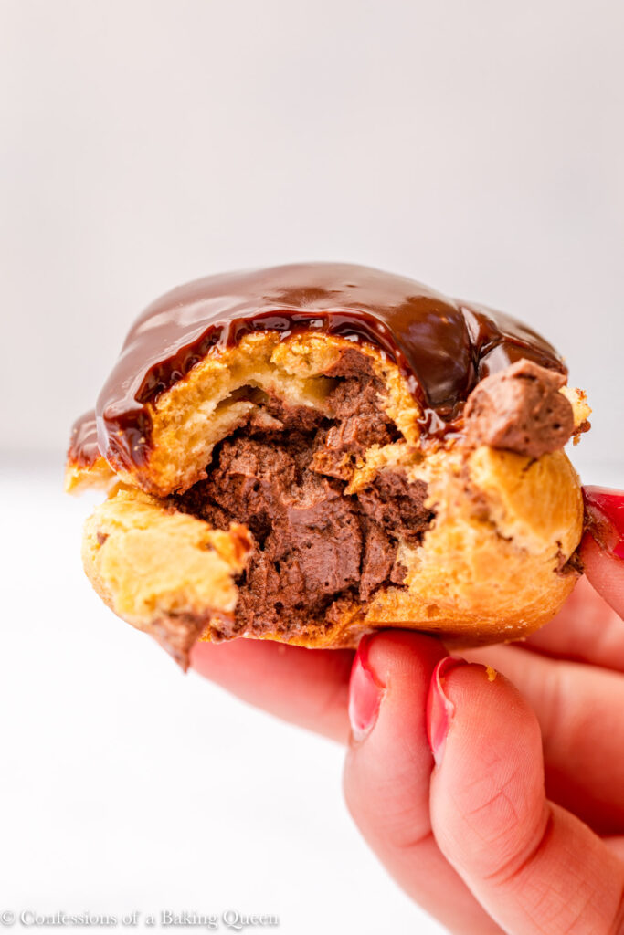 hand holding a chocolate cream puff up close to the camera