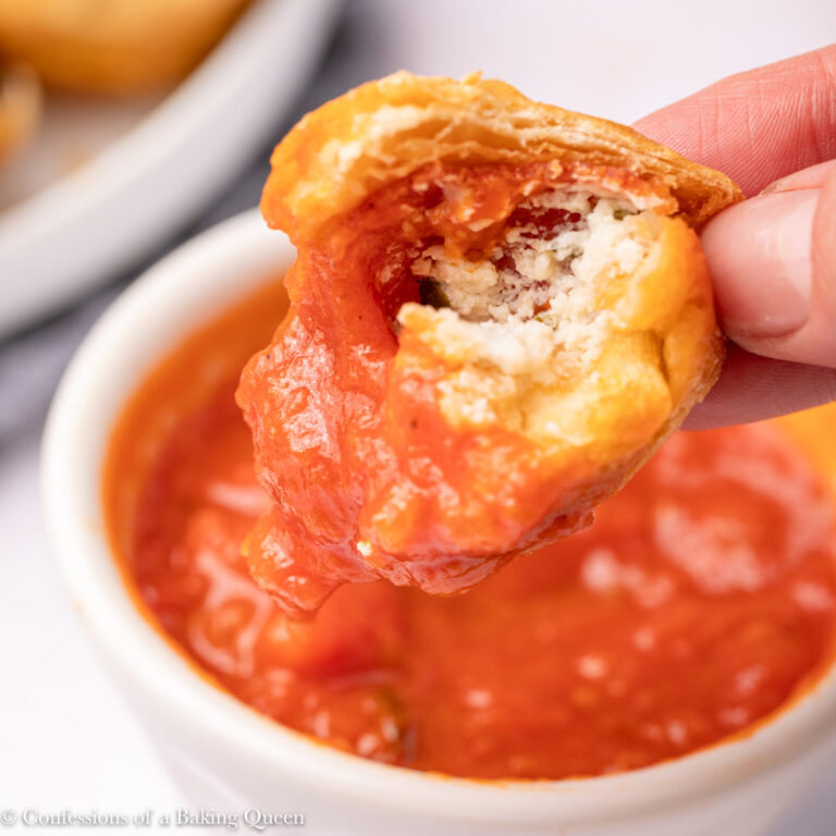 hand dipping a pepperoni pizza puff into marinara sauce on a light pink surface