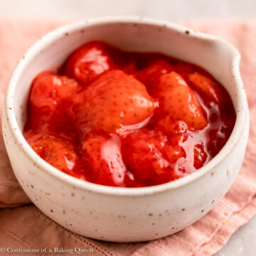 strawberry dessert sauce in a white bowl on top of a pink linen on a white marble surface