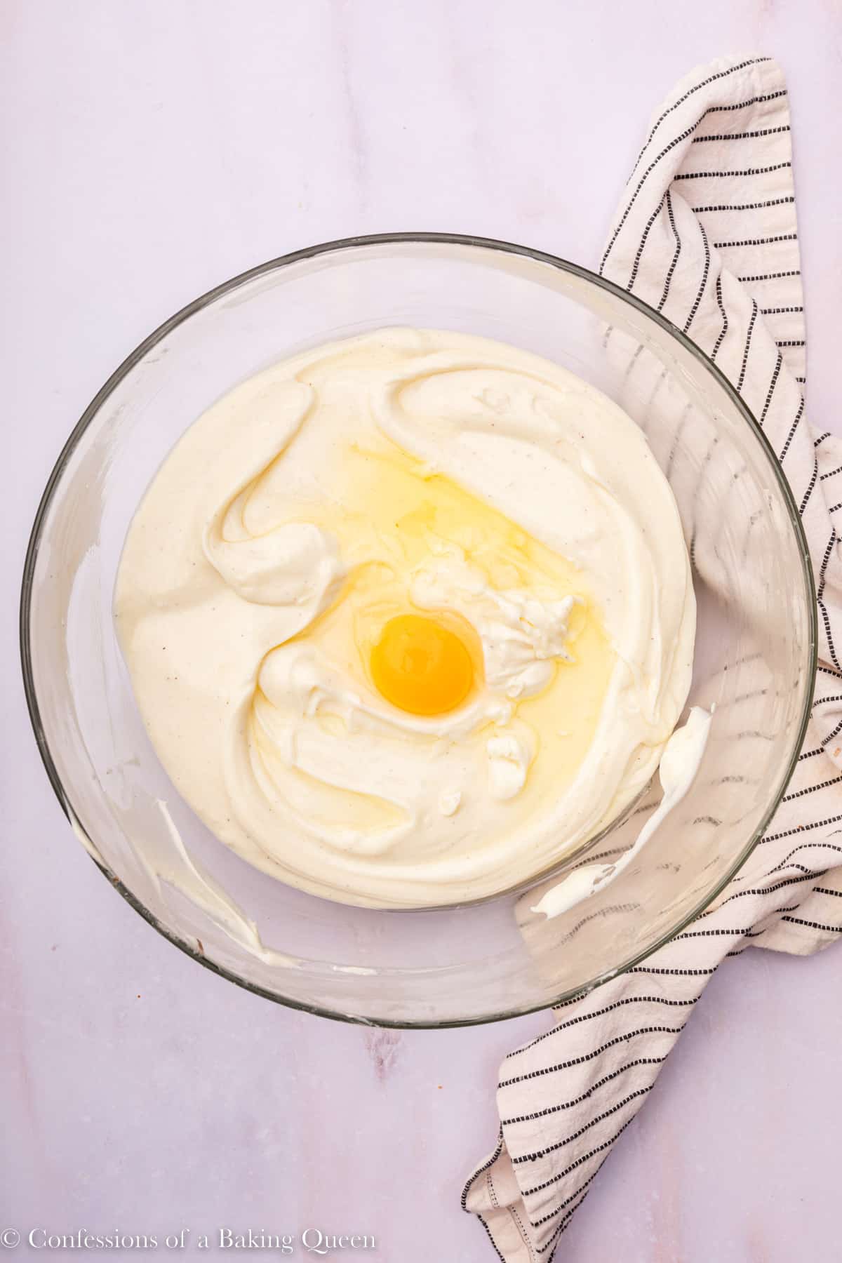 eggs added one at a time to cheesecake batter in glass bowl on a light marble surface with a stripped linen