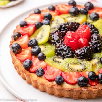 classic french fruit tart on a white plate on top of a pink linen on a light surface