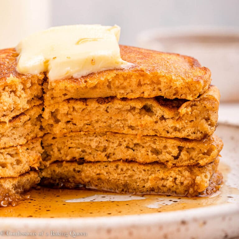 stack of pumpkin pancakes cut into on a white speckled plate on top of an orange linen