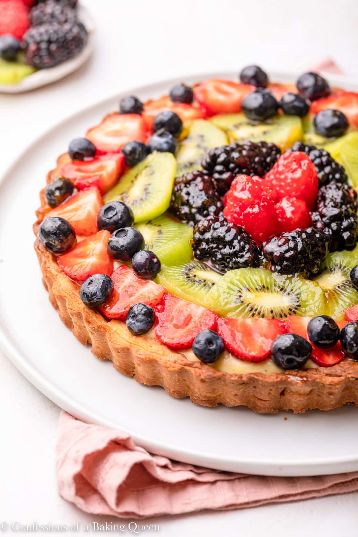 classic french fruit tart on a white plate on top of a pink linen on a light surface