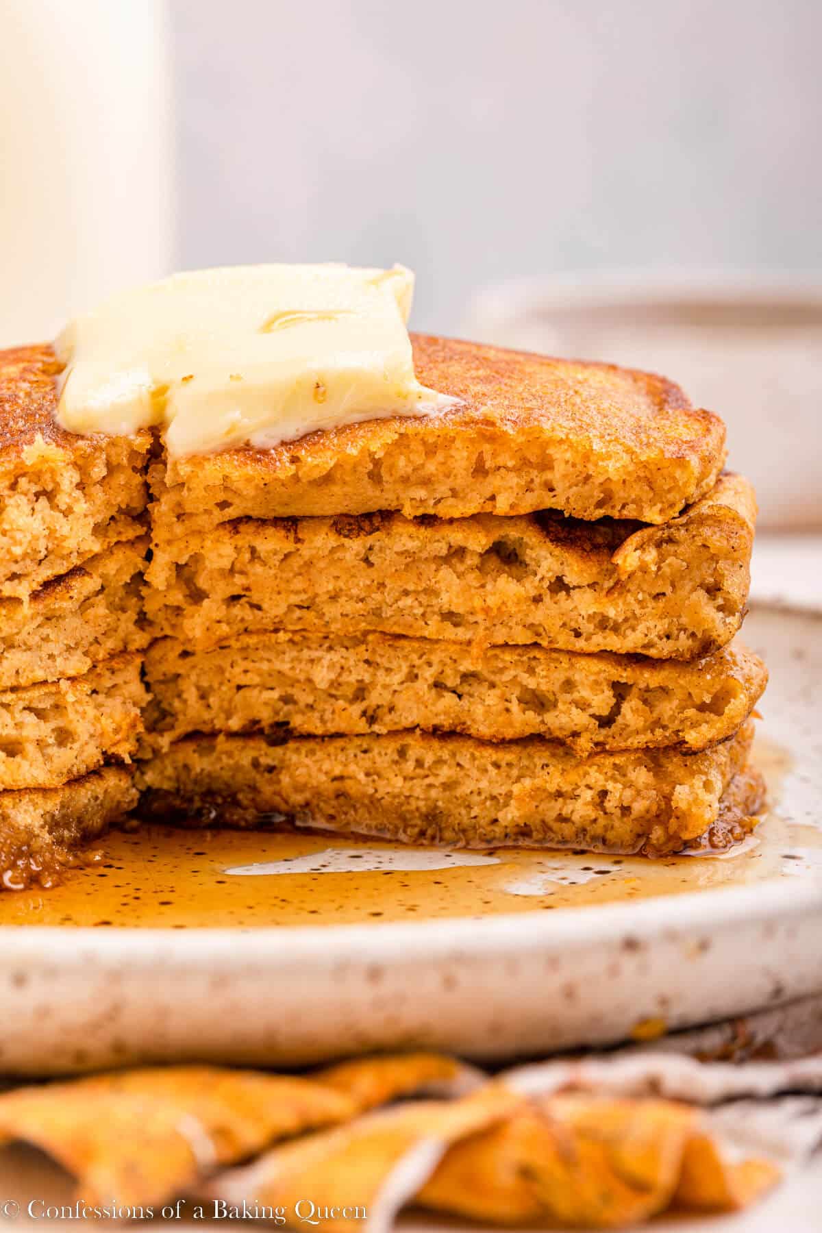 stack of pumpkin pancakes cut into on a white speckled plate on top of an orange linen