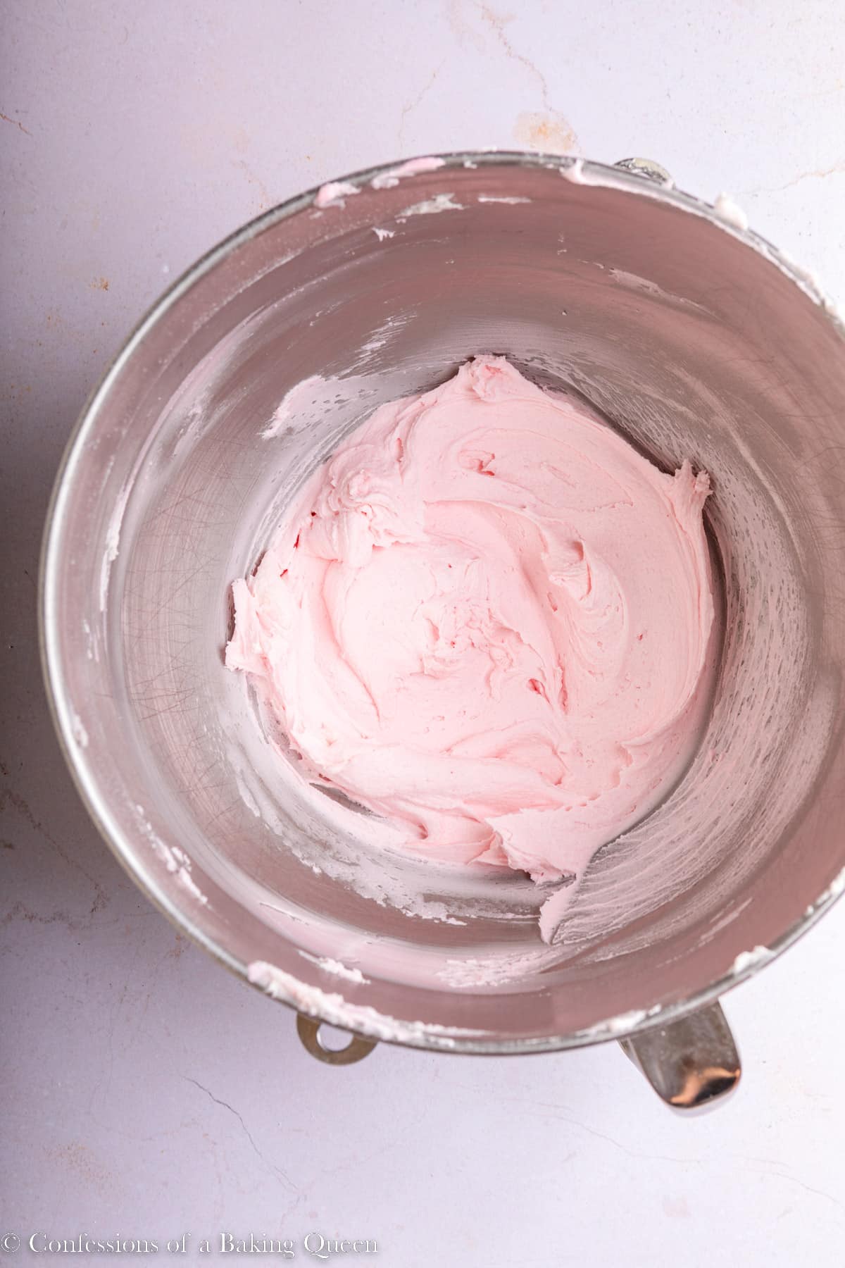 light pink buttercream in a metal bowl on a light surface
