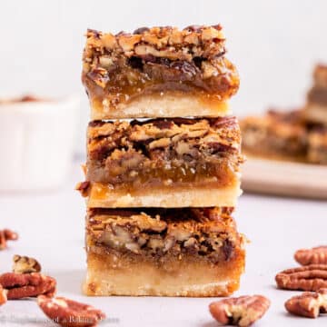 stack of pecan pie bars on a light pink surface with pecans scattered around