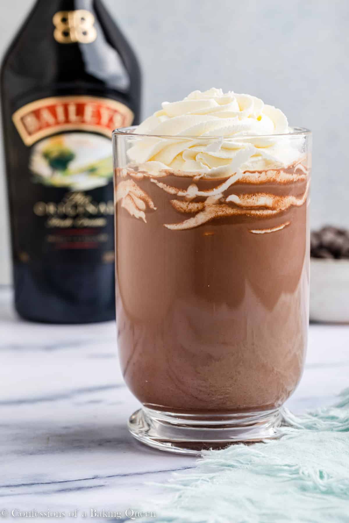 baileys hot chocolate served in a glass mug with whipped cream on a marble surface with a light blue linen