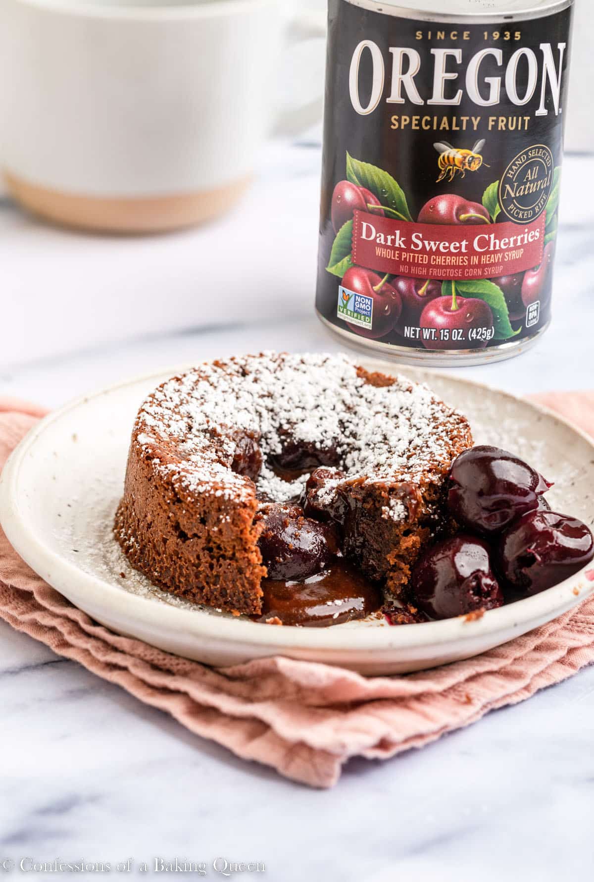 chocolate cherry lava cake served on a plate with a can of cherries in the back with a pink linen on a white marble surface