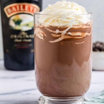 baileys hot chocolate served in a glass mug with whipped cream on a marble surface with a light blue linen
