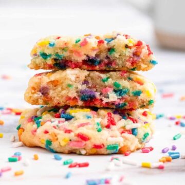 broken funfetti cookies stacked on top of each other on a white surface with a coffee cup in the background