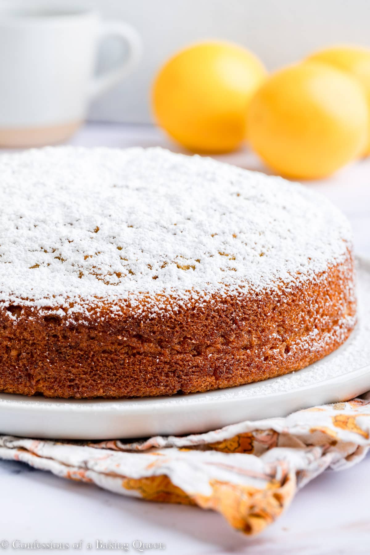 orange olive oil cake dusted with powdered sugar on a marble surface with a floral linen