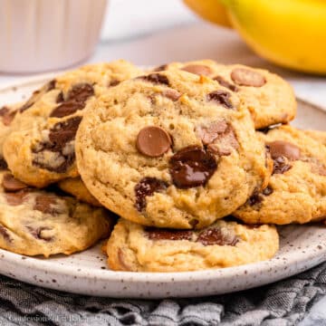 A plate of banana chocolate chip cookies near a bunch of bananas.