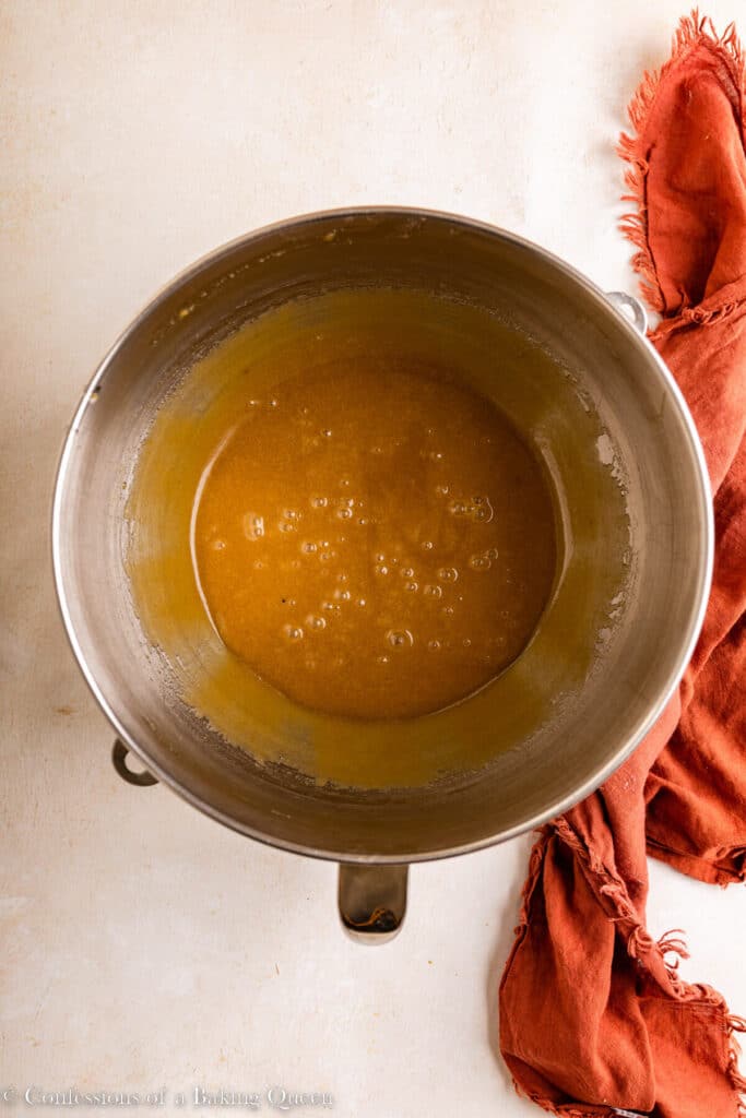 eggs mixed into butter and sugar in a large mixing bowl on a light surface with an orange linen