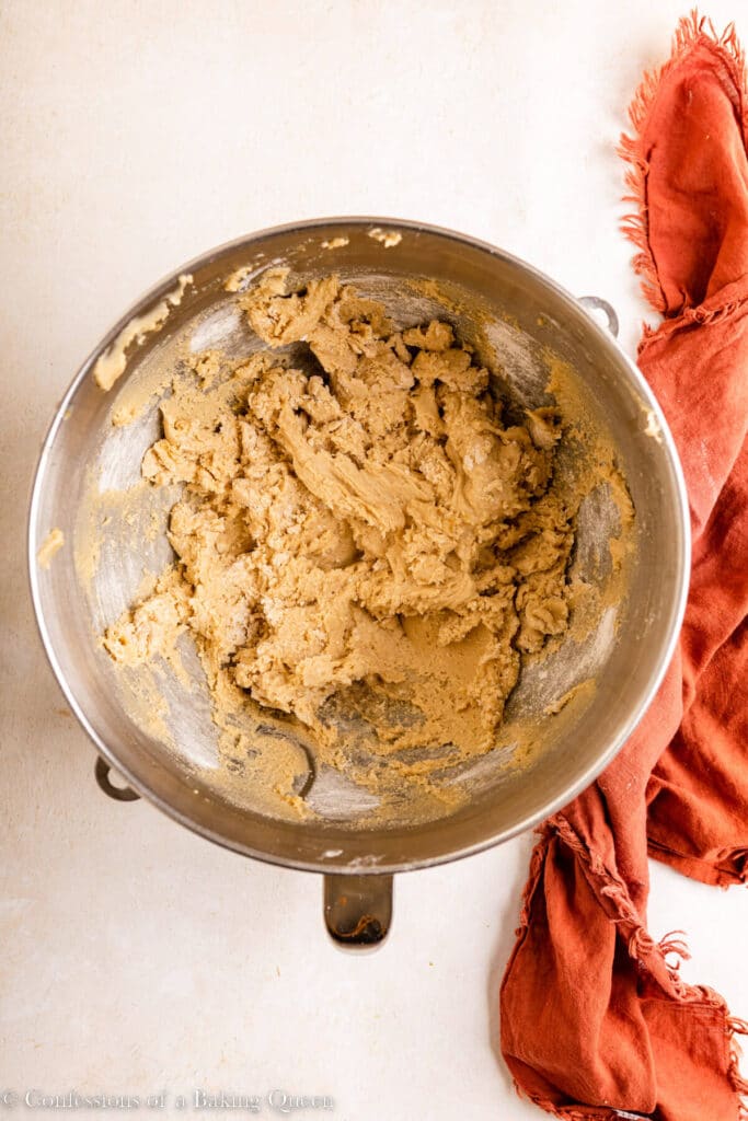 cookie dough in a metal mixing bowl on a light surface with an orange linen