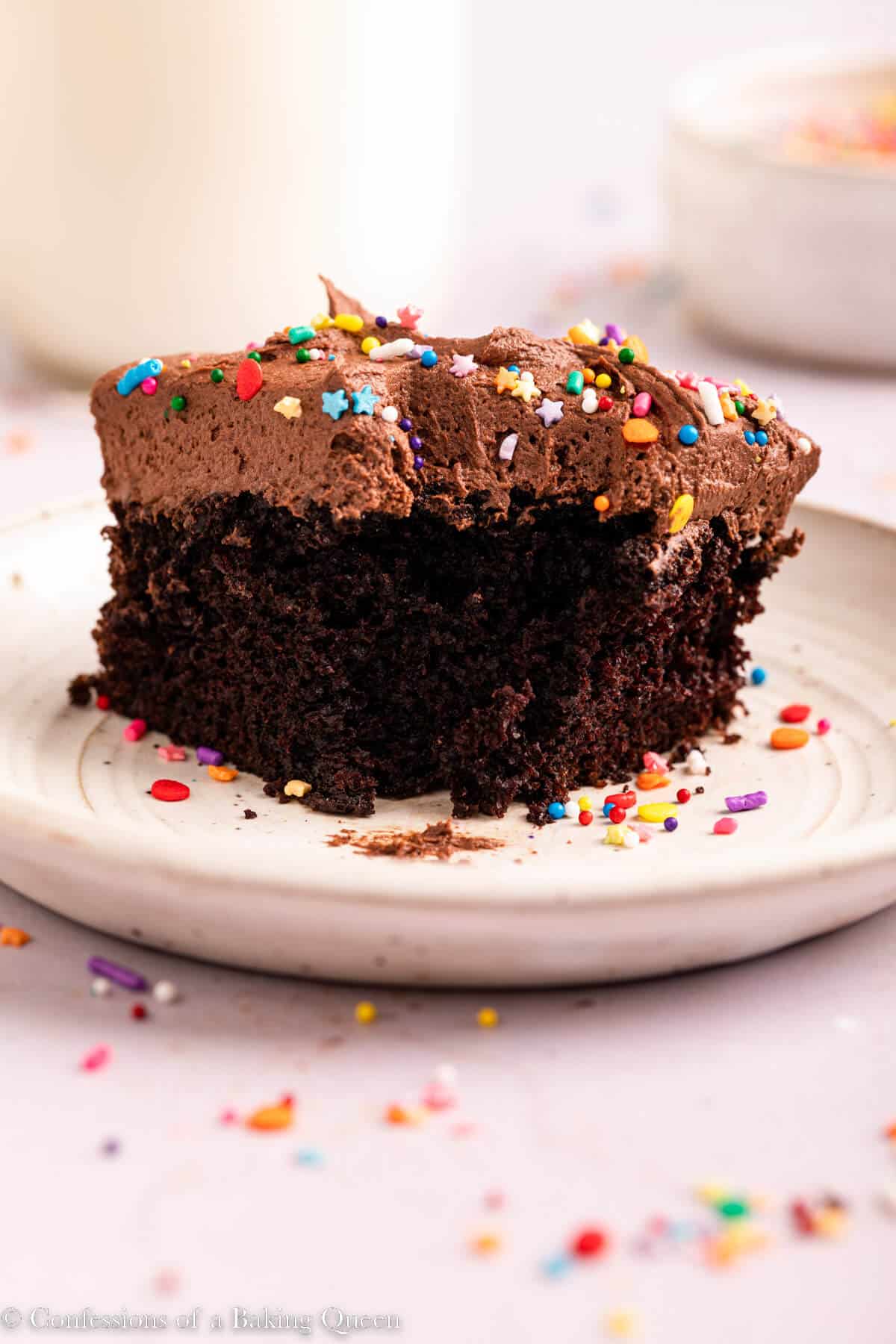 slice of chocolate cake with a bite taken out on a light surface with sprinkles scattered