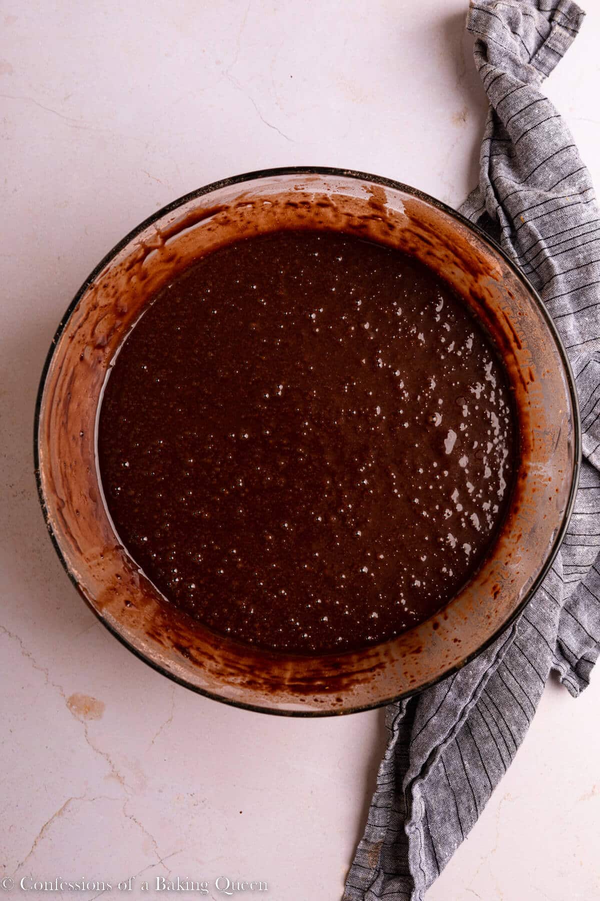 chocolate cake batter in a glass bowl on a light surface with a blue linen