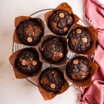 chocolate zucchini muffins cooling on a wire rack on a light surface with a pink linen
