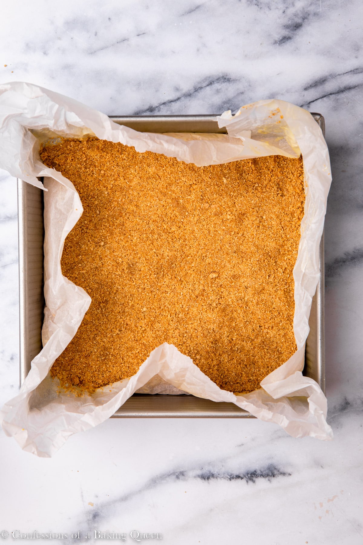 Graham cracker crust for lemon cheesecake bars pressed into a parchment lined baking pan.