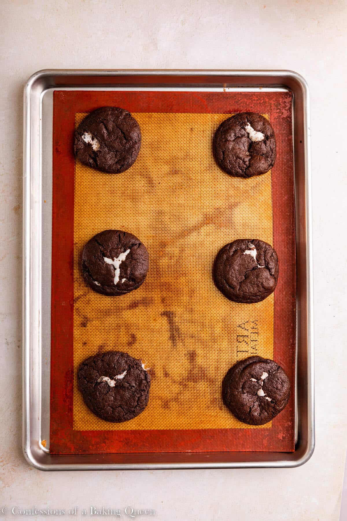 chocolate marshmallow cookies just baked on a silpat lined baking sheet on a light surface