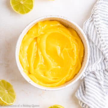 key lime curd in a small white bowl on a light surface with cut up key limes