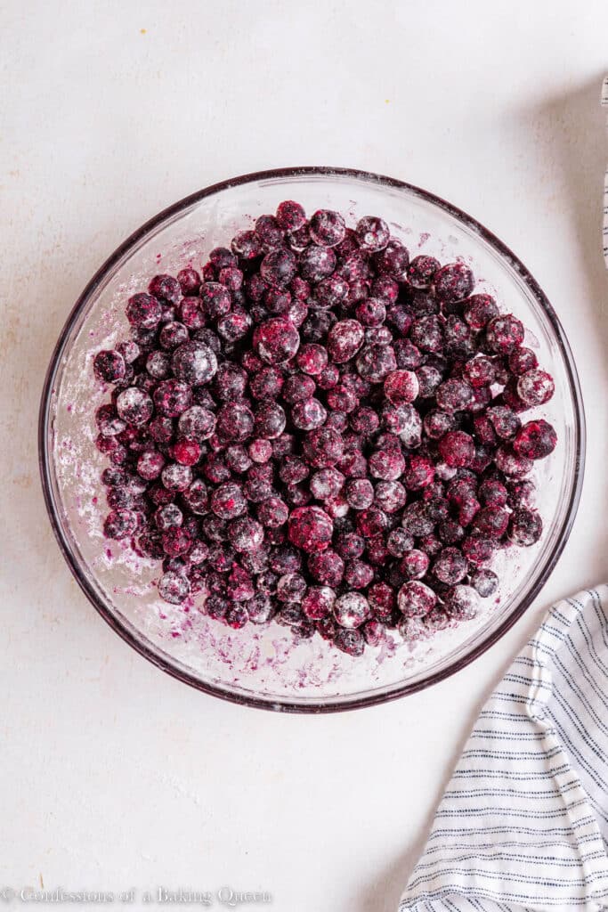 Coating frozen blueberries with flour in a mixing bowl.