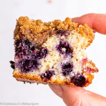 A hand holding a slice of blueberry coffee cake.