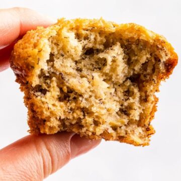 A hand holding a banana bread muffin with a bite taken out of it.