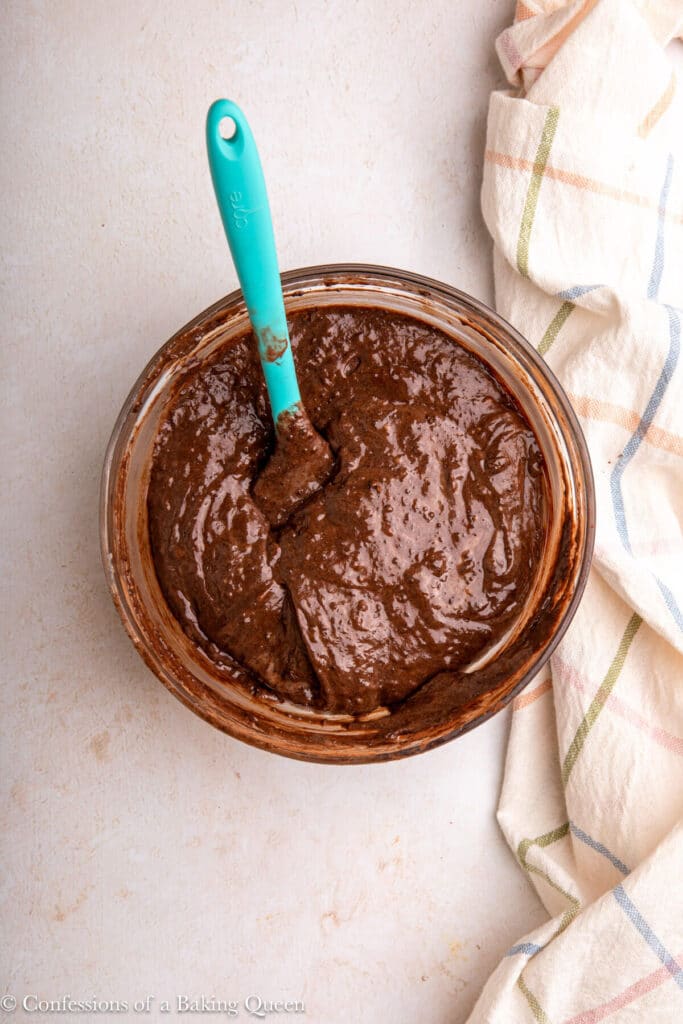 chocolate cake batter in a glass bowl on a light surface with a checkered spring linen