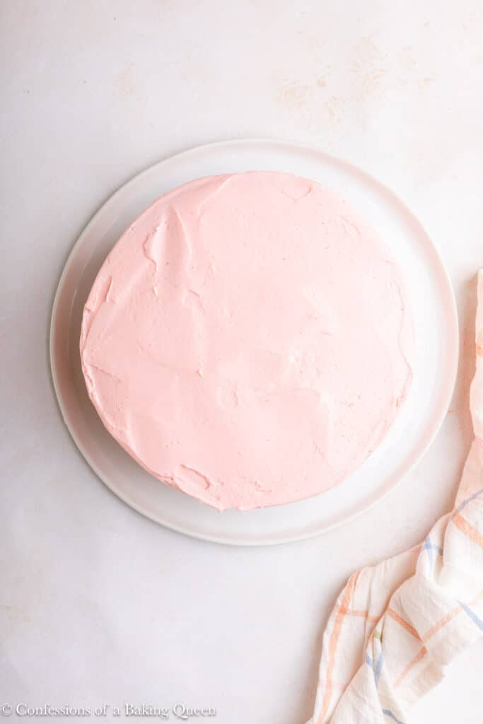 pink frosted cake on a white plate on a light surface with a checkered linen