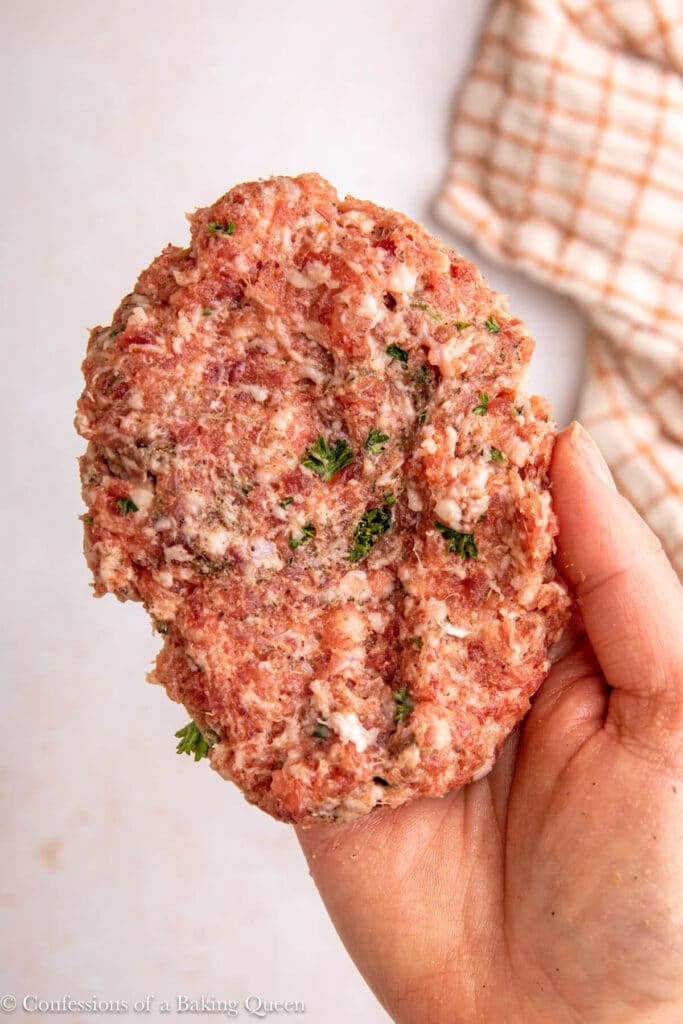 hand holding sausage meat patted out into a large patty