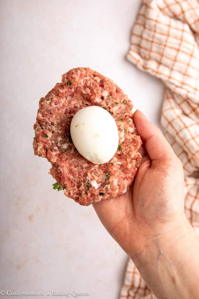 boiled egg on top of a sausage patty held in a hand