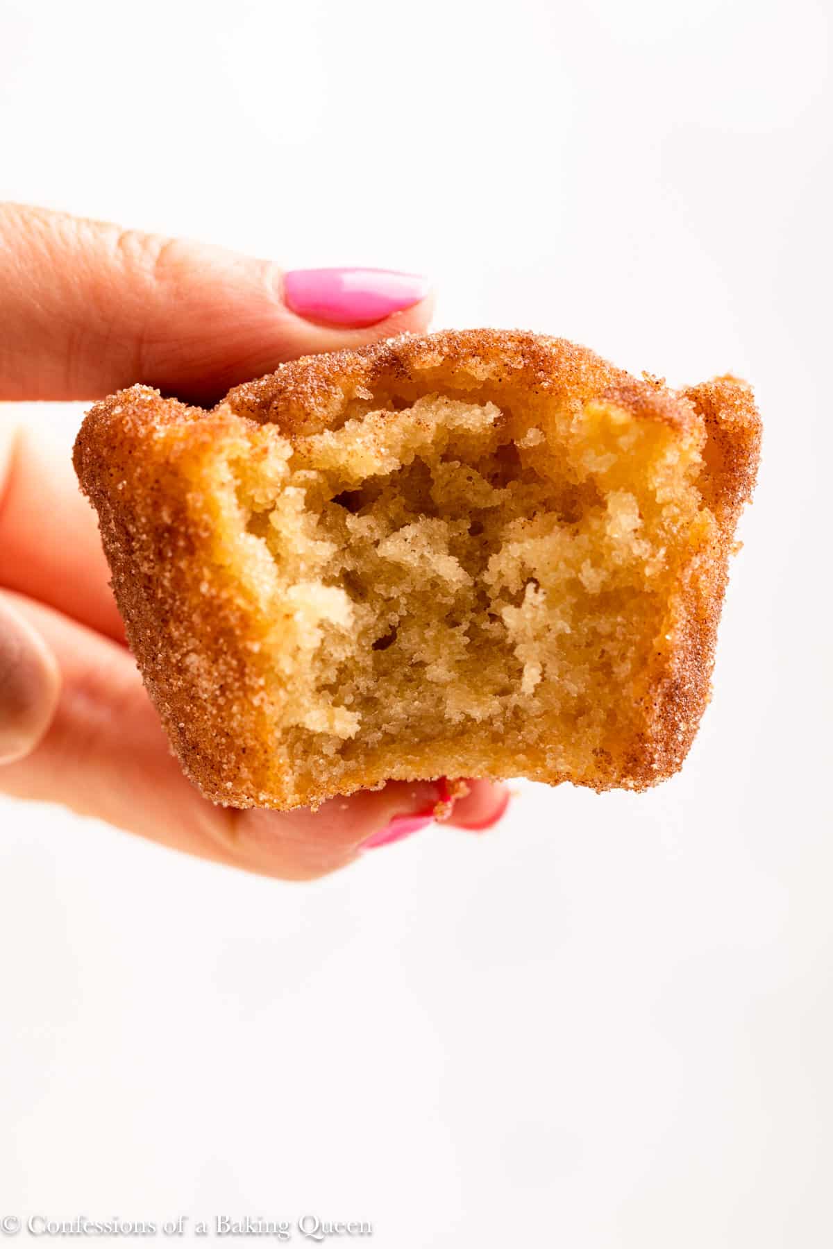 A hand holding a cinnamon muffin with a bite taken out of it.