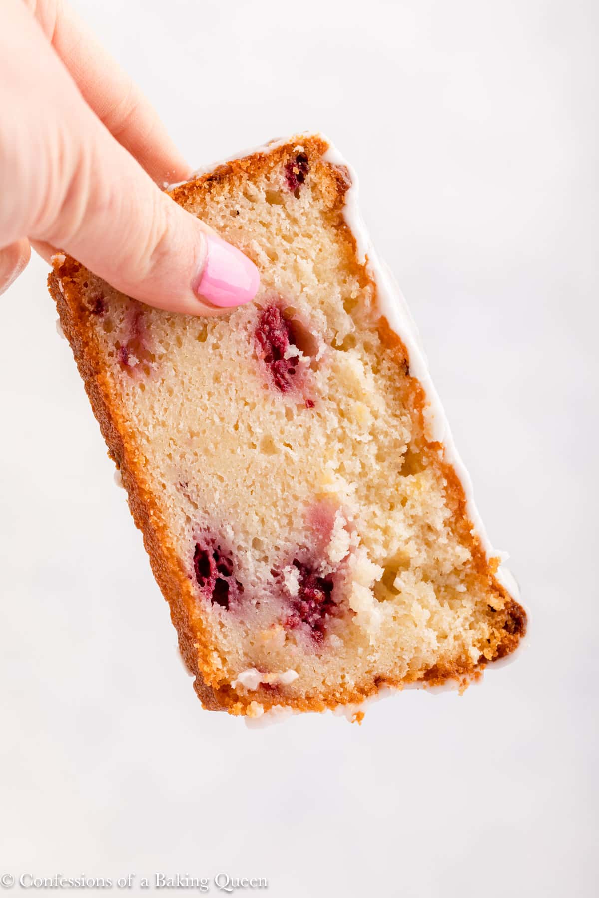 A hand holding a slice of raspberry lemon loaf cake.