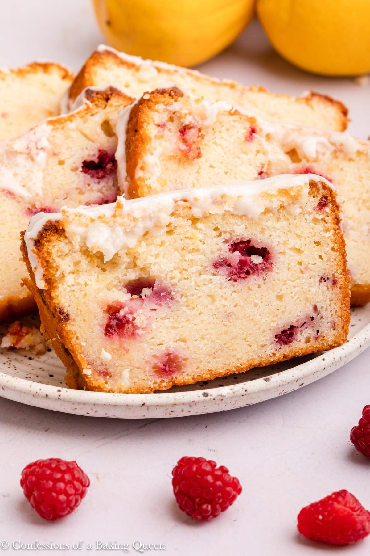 Slices of raspberry lemon loaf cake on a plate near fresh raspberries and lemons.