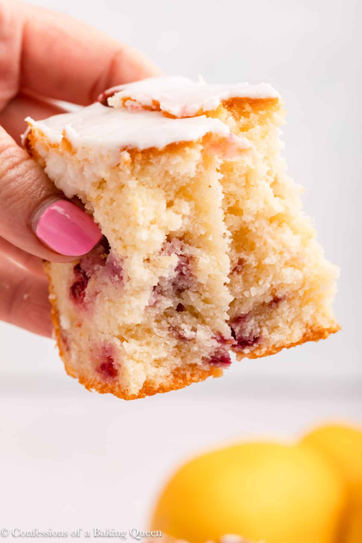 A hand holding a piece of raspberry lemon loaf cake with a bite taken out of it.