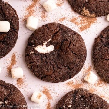 hot cocoa cookies on a light surface with extra marshmallows and hot cocoa powder