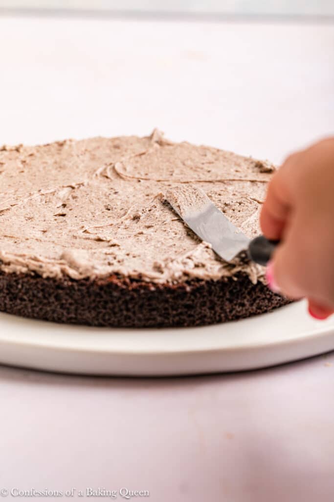 Spreading Oreo cream cheese frosting over a layer of chocolate cake.