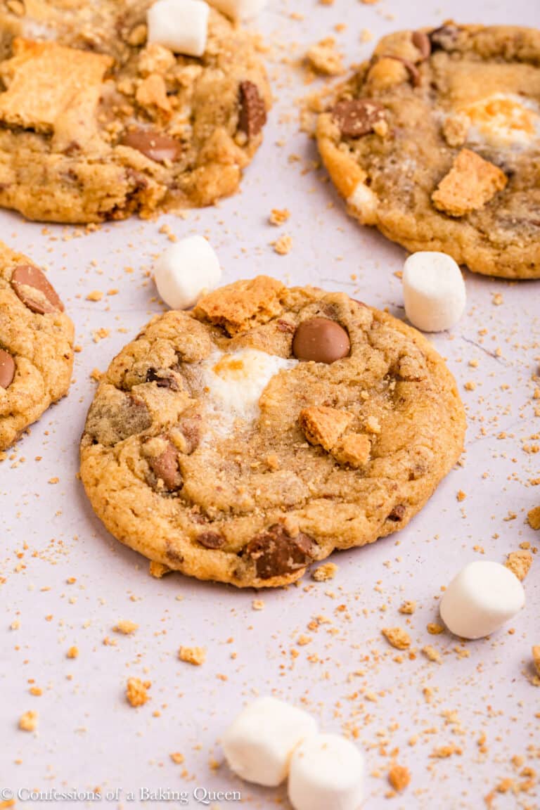 S'mores cookies on a flat surface surrounded by graham cracker crumbs and mini marshmallows.